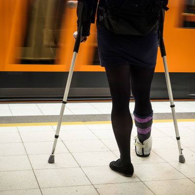 Kyynärsauvoihin nojaava nainen odottaa metroa.