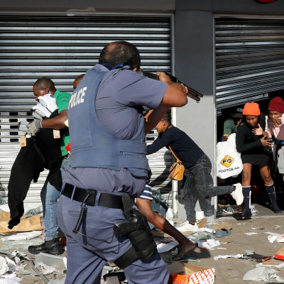 En polis siktar på människor som är i färd med att plundra ett köpcenter i Durban under politiska våldsamheter.
