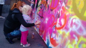 pieni tyttö maalaa seinää spraymaalilla äidin avustamana