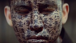 Japaninkielisellä kirjoituksella maalatut kasvot lähikuvassa. Kuva elokuvasta Kwaidan