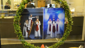 Vissa av bilderna har fått en stor lingonriskrans omkring sig, som en jättelik luciakrona. I ett fönster hänger en stor krans av lingonris. Inuti kransen hänger två förstorade fotografier av lucia med tärnor. Bakom fönstret syns kontorsmiljö.