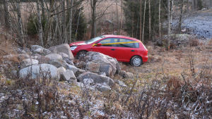 Som tur var verkar de båda passagerarna ha klarat sig utan större skador. En liten röd bil med framändan på en stenhög. Bilen är lite tillknycklad framtill och har ett gult plastband om sig.