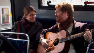 Markéta Irglová ja Glen Hansard. Mies (Glen Hansard) soittaa kitaraa naiselle (Markéta Irglová) bussin penkillä. Kuva elokuvasta Once.