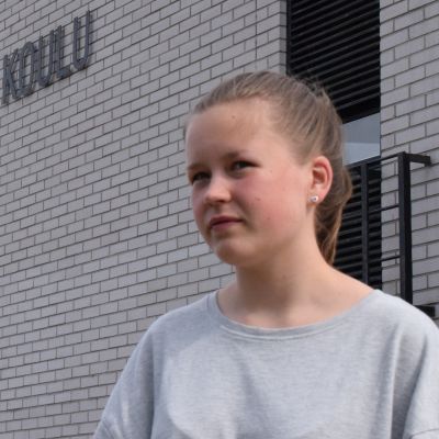 nuori tyttö seisoo ulkona koulurakennuksen vieressä