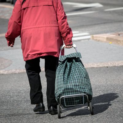 Iäkäs nainen vetää pyörällistä laukkua perässään.