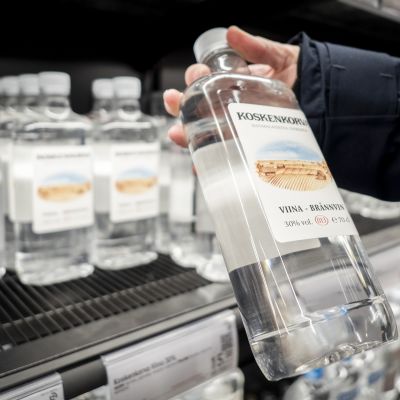 Asikas ottaa alkoholijuomapulloa Alkon hyllystä.