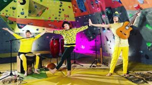 Raka Bananer har spelat in en konsert i en klättringshall Tre musiker står vid en klättringsvägg med sina instrument och tittar in i kameran
