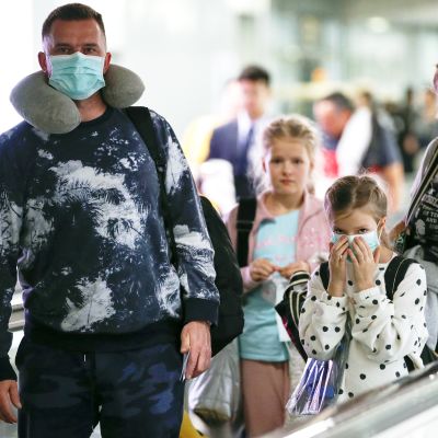 Hengityssuojaimiin pukeutunut perhe Suvarnabhumin lentoasemalla Thaimaassa.