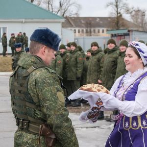 En kvinna i en nationell belarusisk klänning visar upp bröd och salt enligt traditionen i samband med att soldater anländer till sina posteringar .