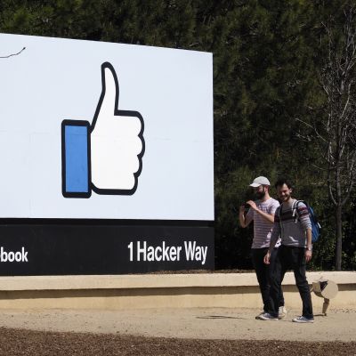 Kaksi nuorta miestä kävelee Facebookin tutun peukutuskuvataulun ohi.