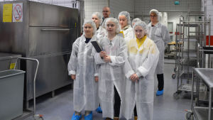 Borgbyflickorna fick bekanta sig med centralköket i Sibbo. Från vänster till höger: Helene Erlund, Ada Ullberg, Miranda Krogell, Ida Stenfors och Kiara Federley. Bakom dem står bespisningsförman Markus Manner och Borgby skolas rektor Desirée Wirén. sju barn och två vuxna står i ett storkök. De har på sig vita engångs-skyddsrockar, vita skyddsmössor och blå plastskydd ovanpå skorna.