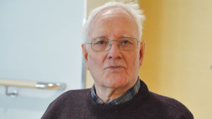 Sigfrid Ahlberg bor själv inte i Majberget men besöker ofta sin hustru på servicehemmet där. Närbild på en äldre man som tittar in i kameran. Bakom honom syns en vit vägg och en träfärgad dörr.