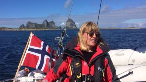 Linda Karlsson utanför ögruppen Træna som ligger på Helgelandskusten i Nordland fylke. Linda Karlsson på en segelbåt med norska flaggan och höga berg i bakgrunden.