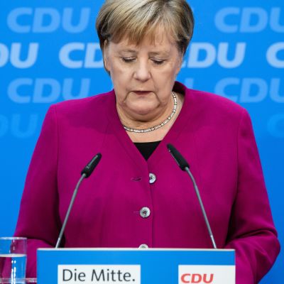 Puolikuva Angela Merkelistä violentinpunaisessa jakussa, katse alaspäin luotuna.