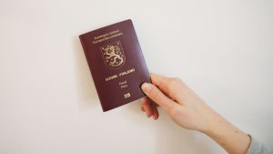 En hand håller i ett finskt pass mot en ljus vägg.