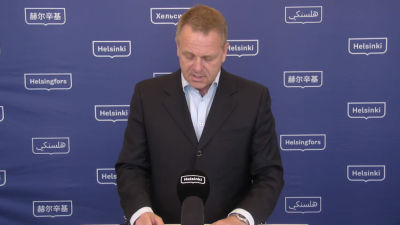 Kostymklädd man i medelåldern som läser från ett papper och pratar i en mikrofon.