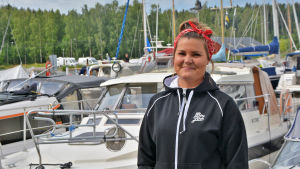 Linda Pirtelä En ung kvinna i svart luvtröja står framför flera båtar. Hon tittar in i kameran och ler.