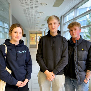 Tre gymnasiestuderande står i en korridor.