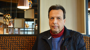 Tuomo Ravi är också lite skeptisk till bostadsmässan. En medelålders man sitter på en bänk inne i en restaurang.