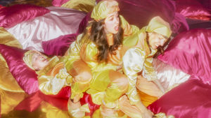 Nadja Hjorton, Lisen Rosell och Amanda Apetrea släpper hämningarna och låter sig svepas med av romantiska fantasier. Tre kvinnor i Harlekindräkter sitter ovanpå varandra bland rosa och röda sidenkuddar.