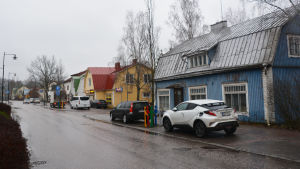 En hel rad med trähus kantar ena sidan av Stora Byvägen. Det blå huset närmast kameran är Rosenholms hus och det gula bredvid det är Singsing. Stora Byvägen i Nickby. En gata kantas av höghus på vänstra sidan och trähus i blått, gult och vitt på högra sidan.