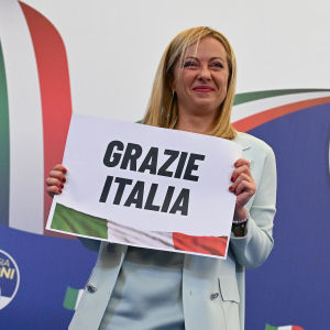 Giorgia Meloni står på en scen och håller i en skylt där det står "tack Italien".