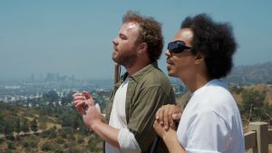 Brian Bushway ja Sean Ricks seisovat kukkulalla ja kuuntelevat maisemaa taputtamalla käsiään yhteen. Taustalla on Los Angelesin kaupunki.