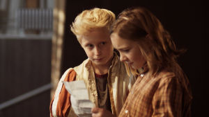 Young Love. Sune och Sofie (Lily Wahlsteen). Sune och Sofie bredvis varandra med ett betydelsefullt papper i handen.