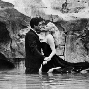 Mies ja nainen (Marcello Mastroianni ja Anita Ekberg) seisovat täysissä pukeissa reisiä myöten vedessä, taustallaan veistoksellinen kallioseinämä. Kuva elokuvasta La dolce vita - ihana elämä.