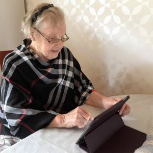 Lena Dalvik hör till de äldre som gärna använder digital teknik för att hålla kontakten med nära och kära. Hon har två mobiltelefoner, en dator och en surfplatta som hon använder för att ringa barn, barnbarn och barnbarnsbarn. Äldre kvinna ser på en surfplatta