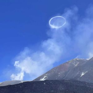 En rökring stiger från en vulkan mot en blå himmel.