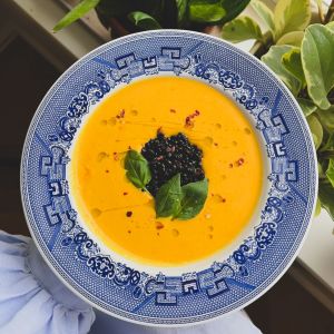 En blåvit tallrik med orange morotssoppa toppad med svarta belugalinser.