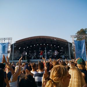 Publikhav framför utomhusscen en varm sommardag. Många klappar och viftar med händerna.