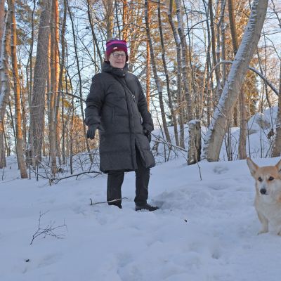 Nainen ja koira lumisessa maisemassa.
