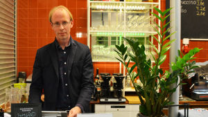 Mika Myllynen står ofta bakom kassan. "Jag försöker hålla mig undan från köket för att inte vara i vägen", skojar han. En man i svarta kläder står bakom disken i en restaurang.
