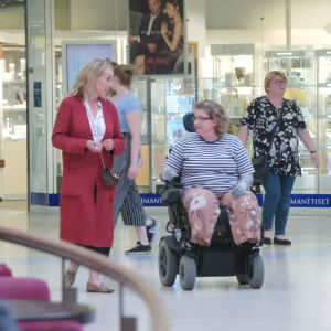 Stylisti Outi Broux kävelee kauppakeskuksessa pyörätuolilla kulkevan naisen rinnalla.