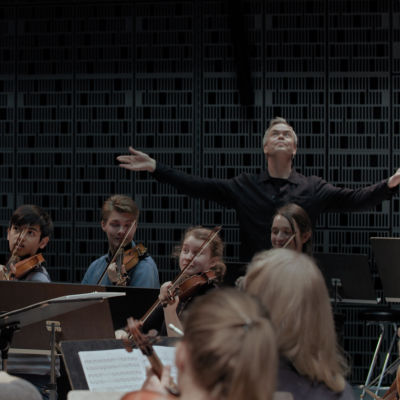 I-Han Fu dirigerar och Hannu Lintu slår ut med armarna bakom orkestern.
