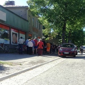 Mellan 70 och 120 personer brukar vänta på att mathjälpen öppnar sin utdelning. Folk köar utanför en tidigar mataffär där en förening delar ut mathjälp i Karis. Sommar. Bilar och cyklar syns också.