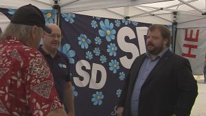 Richard Carlsson (SD) hoppas att M ska börja diskutera med SD, men hittills har det varit trögt, menar han. Richard Carrlsson talar med två män i Sverigedemokraternas valtält.
