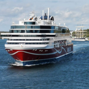 Viking Linen punavalkoinen Glory-alus poistumassa Maarianhaminan Länsisatamasta, poutainen sinitaivas, meri, taustalla Pommern-purjelaiva ja satamaterminaali.