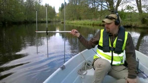 Forskarna följde radiosignalerna från fiskarnas sändare. På bilden forskaren Juha-Pekka Vähä. En man i en roddbåt med en antenn i sin hand och hörlurar på öronen. Han heter Juha-Pekka Vähä.