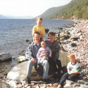 Nuoret vanhemmat kolmen pienen lapsensa kanssa skotlantilaisessa järvimaisemassa Loch Nessillä.