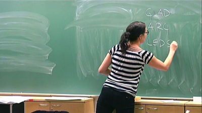 En kvinna skriver på en tavla i ett klassrum.