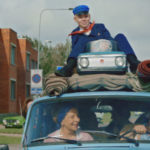 Pojken Johannes sitter på det fullpackade biltaket medan hans familj sitter inne i bilen och kör. 