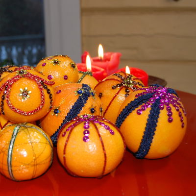 Eb röd bricka med mandariner och apelsiner som dekorerats med paljetter och sidenband i olika färger.