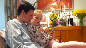 Maarit tillsammans med sitt 6-åriga barnbarn Melissa. Maarit Feldt-Ranta sitter i en fåtölj med sitt barnbarn i famnen.