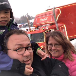 Lyckan är att få vara en familj. Samantha, Mikael Nordmyr och Anneli Heikkilä-Nordmyr. Tre personer framför en Coca Cola långtradare. Två vuxna och ett barn som sitter på en mans axlar.
