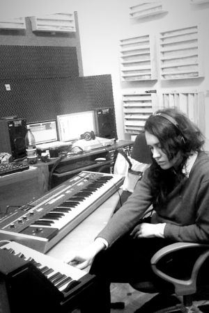 Ozeran i sin studio. Artisten Chikiss sitter i rum fullt av synthar och skärmar och gör musik. Mörkt hår, hänger ner, Ansiktet i halvbild.