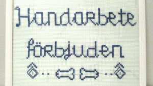 Konstverk om åldrande och självbestämmanderätten. Korsstygnsbroderi som säger "handarbete förbjuden".