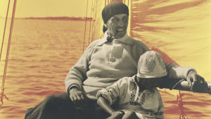 En man och ett barn i en segelbåt. Mannen har en pipa i munnen.